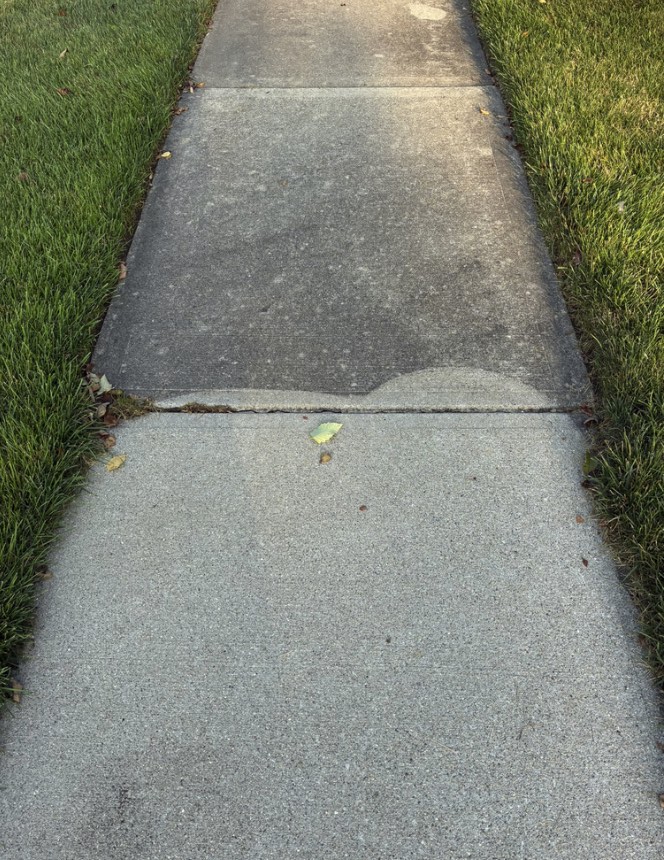 Sidewalk in Carmel, IN halfway through pressure washing — dull gray concrete above the line, bright clean concrete below it